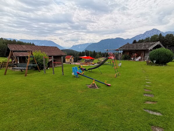 A playground with swings and slides, surrounded by houses and mountains. - Apartment - 4 persons+, 70sqm, 2 bedrooms, balcony, eat-in kitchen, unique location, WLAN (Anger)