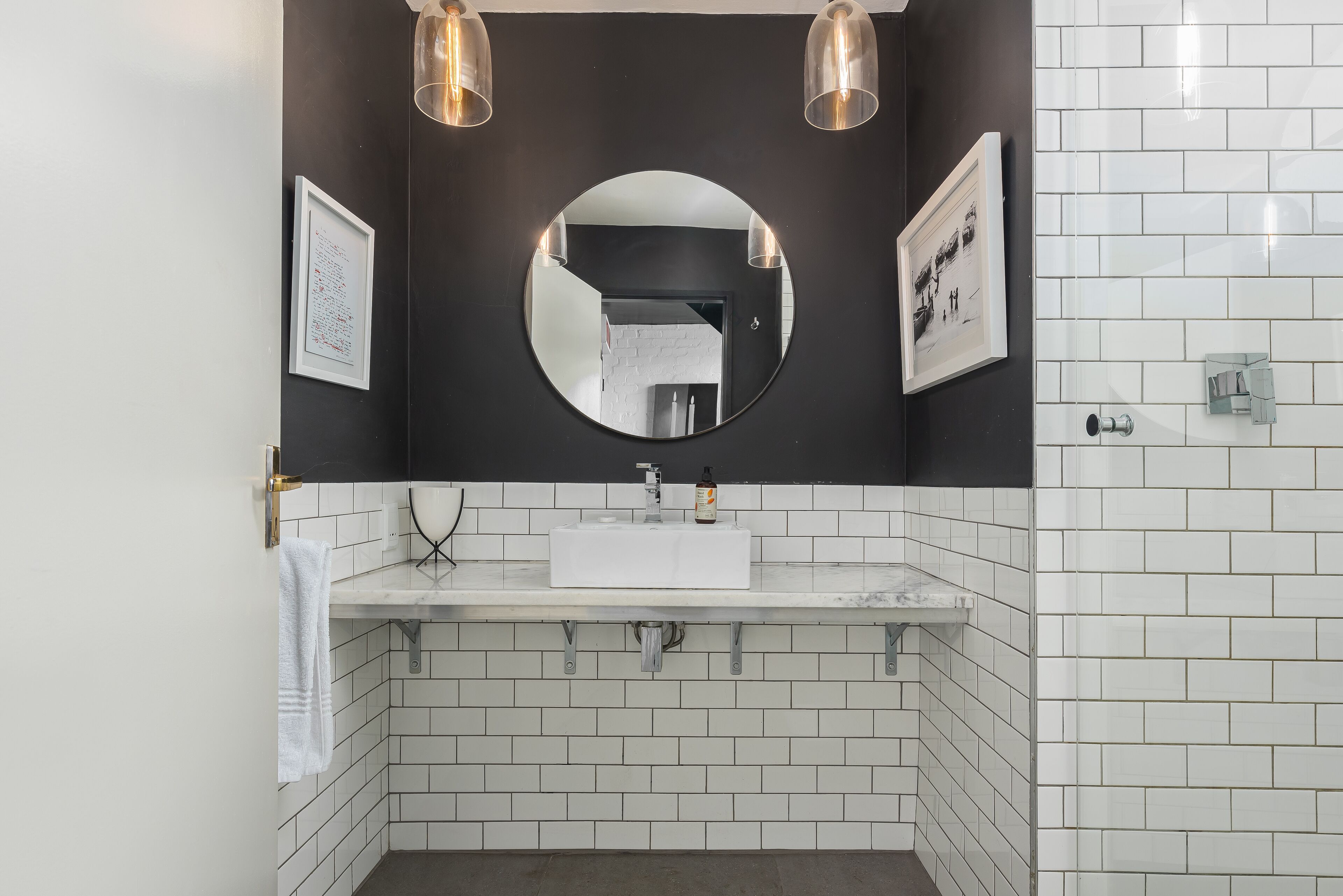 A modern bathroom with a white sink, a round mirror, and two pendant lights.