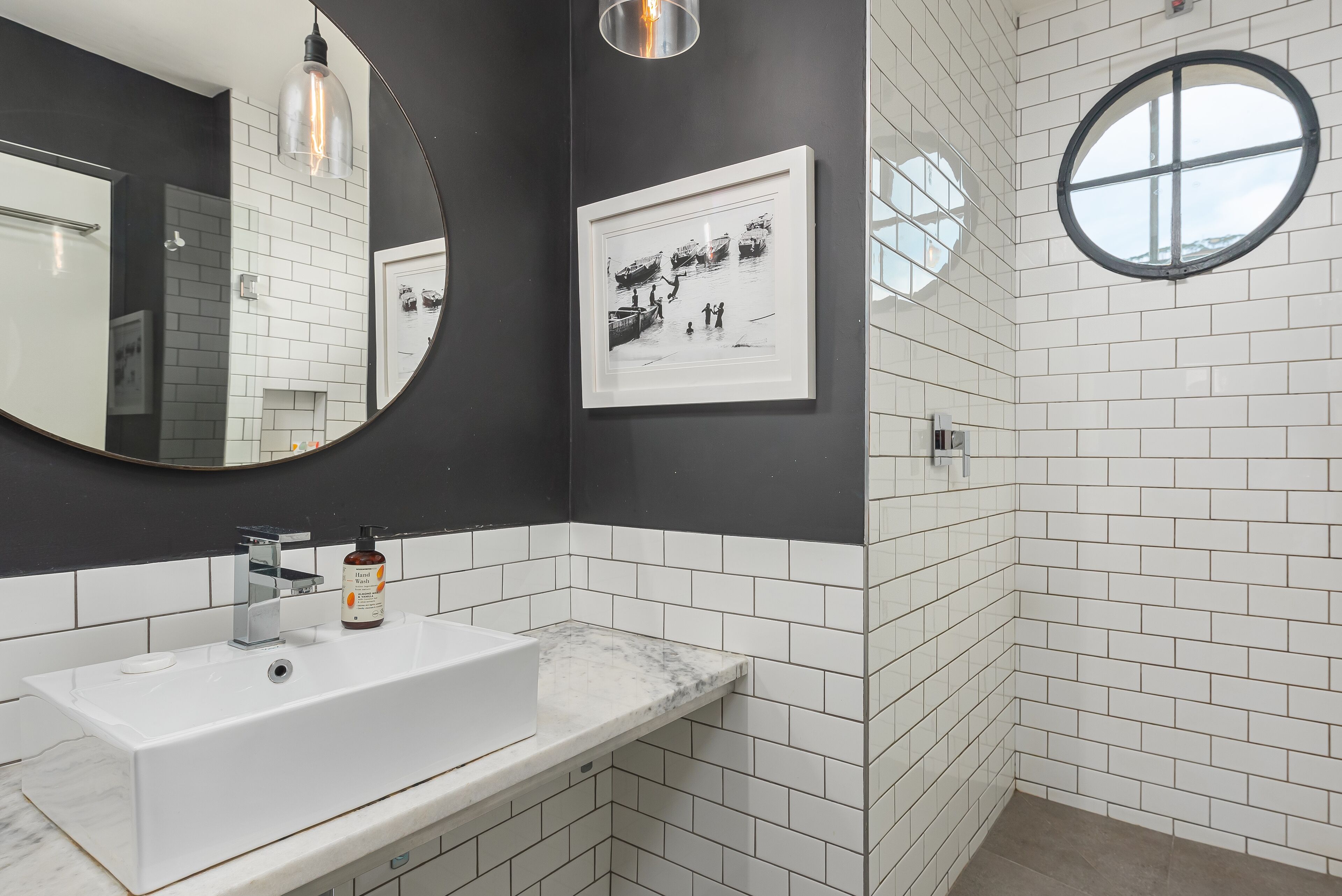 A bathroom with a white sink, a large mirror, a framed picture on the wall, and a round window.