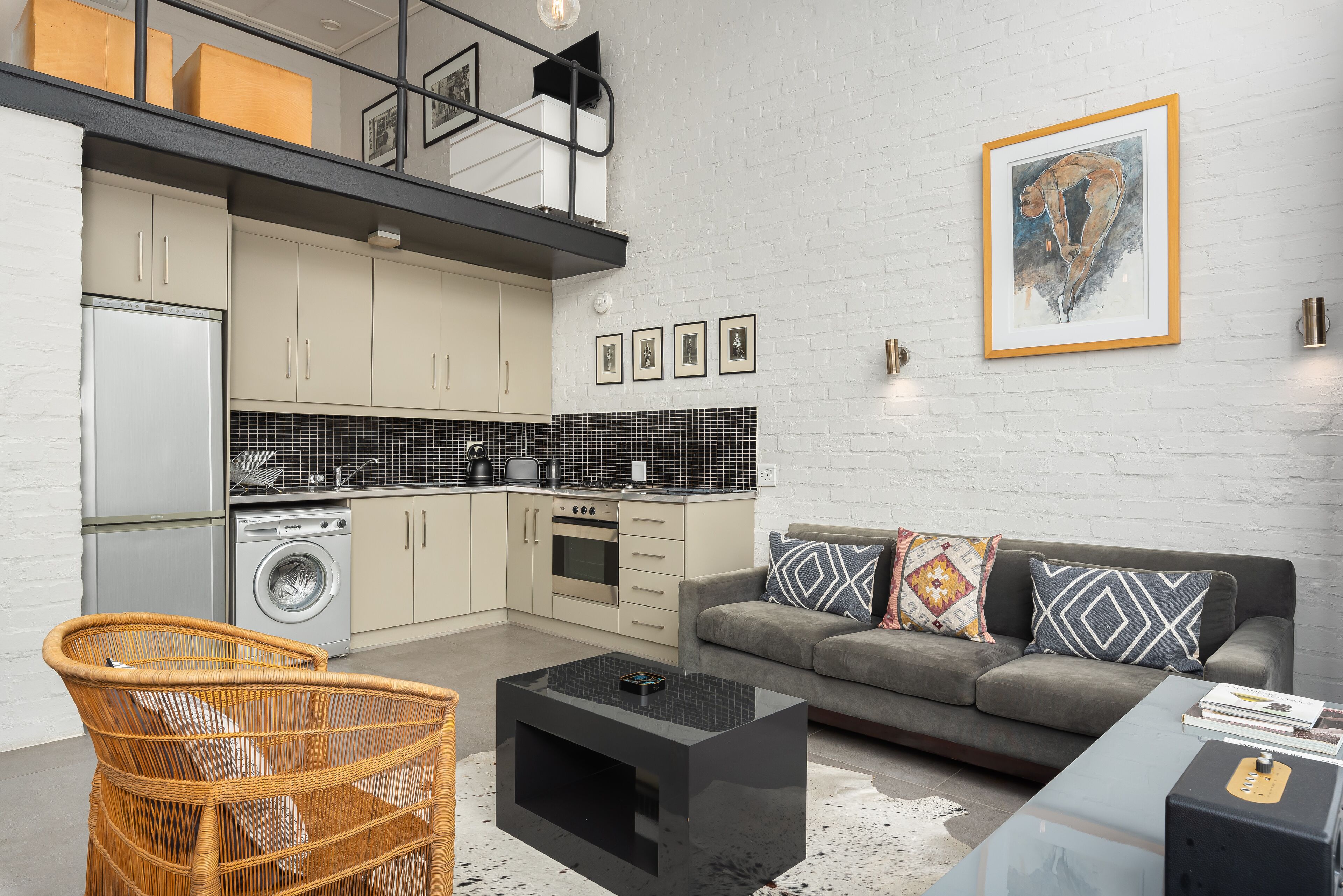 A modern kitchen with a built-in oven, a washing machine, and a dining area with a sofa and coffee table.