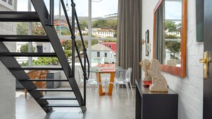 Ein modernes Interieur mit einem Glastisch, klaren Stühlen, einer Holzkommode und einer schwarzen Metalltreppe.