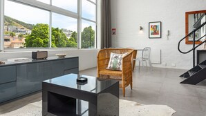Ein modernes Wohnzimmer mit großem Fenster, einem Korbsessel, einem Glastisch und einer Treppe.