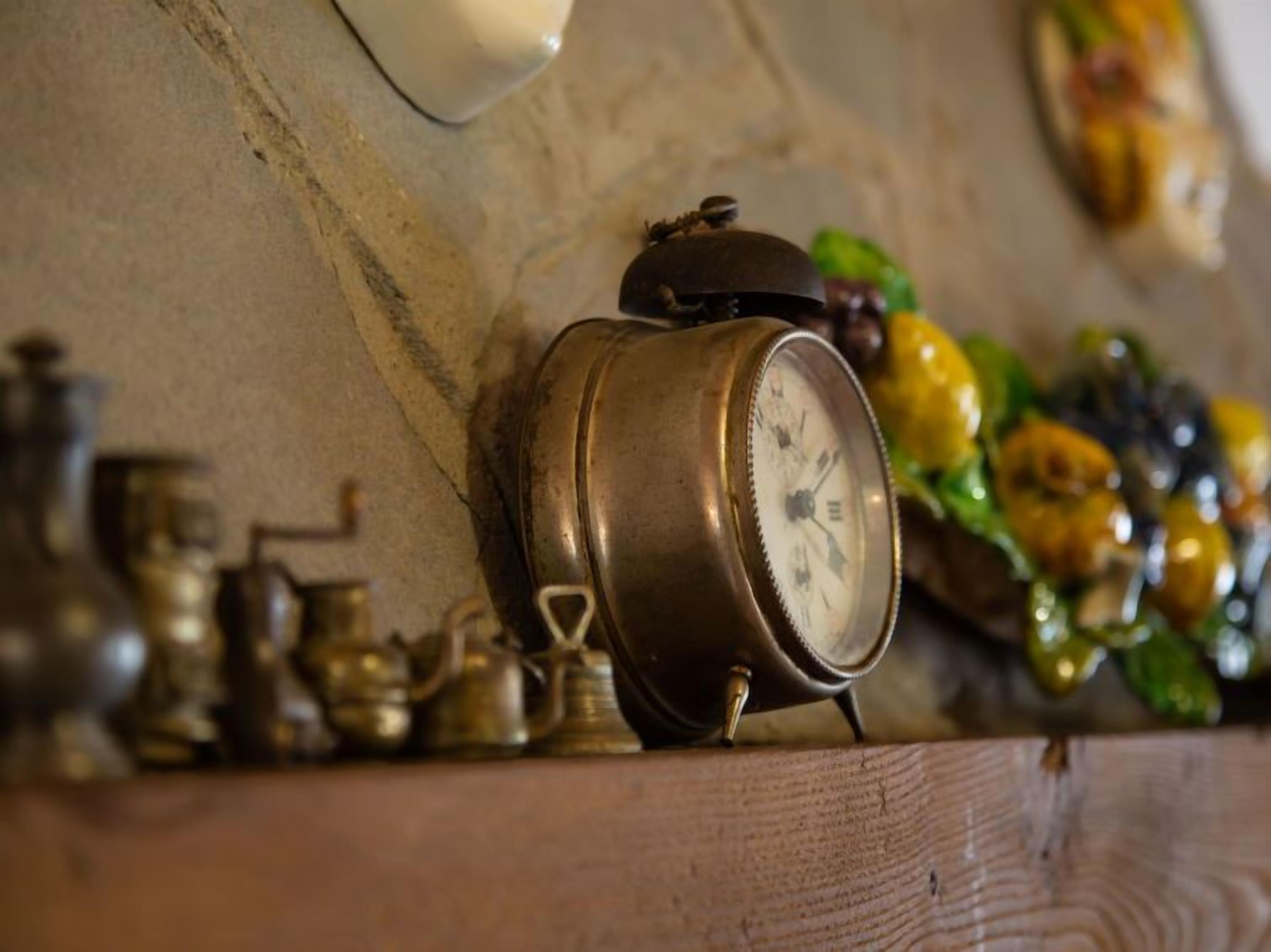 A brass clock on a wooden shelf with a wall clock above it.