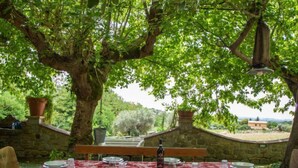 Ein Essbereich im Freien mit rot-weißer Karomuster-Tischdecke, umgeben von Steinmauern und großen Bäumen.