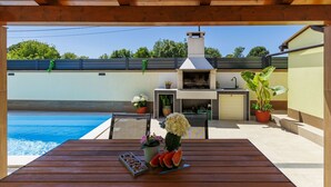 An outdoor patio with a wooden table, a barbecue grill, and a pool. - Vacation home Laura by Interhome (Štinjan)