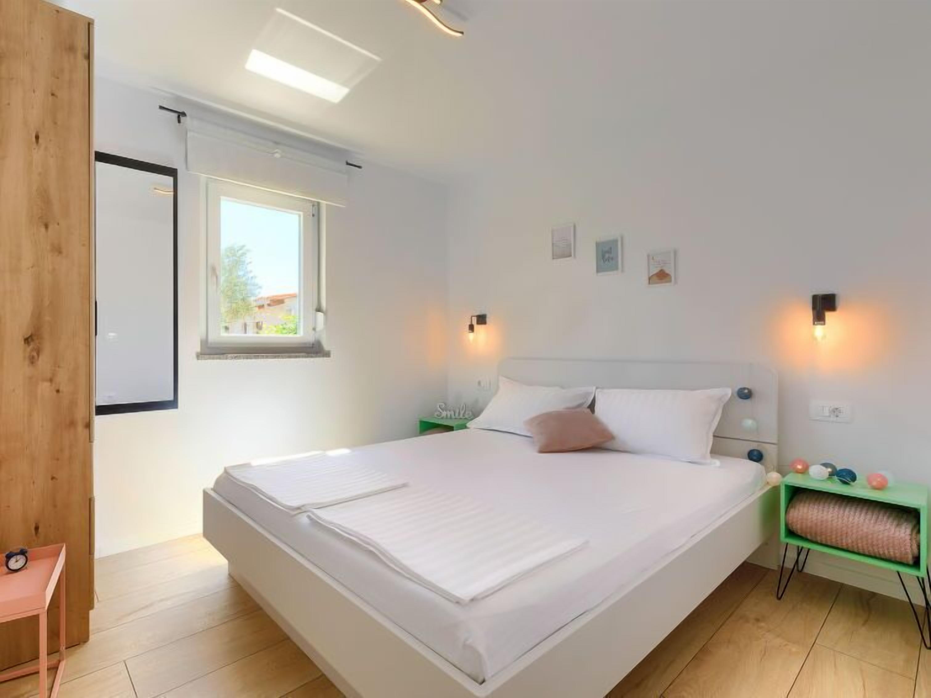A bedroom with a large bed, a window, two bedside tables, and a green nightstand.