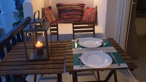 A balcony with a dining table set for two, a candle, and a colorful striped cushion.