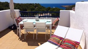 A terrace with a table and chairs, a colorful striped cushion, and a view of the sea.