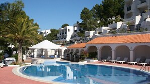 A swimming pool with lounge chairs, a gazebo, and white buildings with red-tiled roofs.