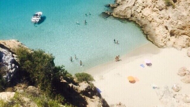 A coastal area with clear turquoise waters, rocky terrain, and a sandy beach.
