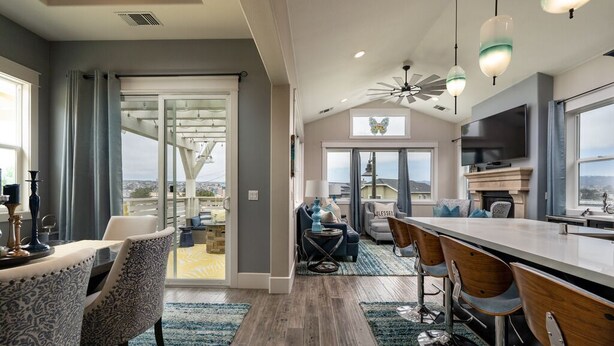 A spacious living area with a large window, a ceiling fan, and a bar area with stools.