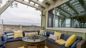An outdoor seating area with a stone fire pit, wicker furniture, and a pergola with hanging lights.