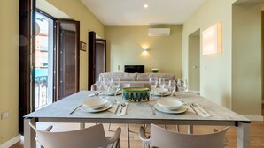 A dining area with a table set for four, a sofa in the background, and a TV mounted on the wall.