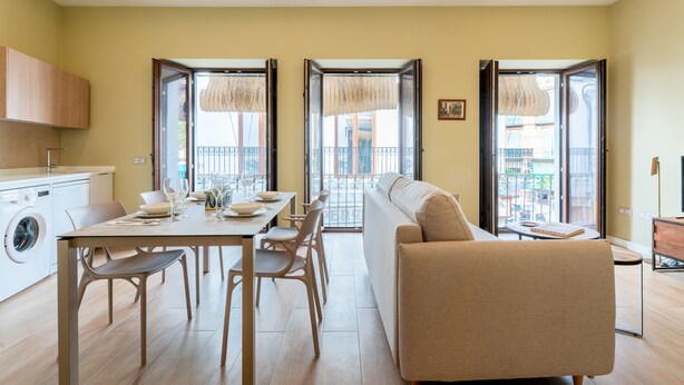 A modern living room with a sofa, dining table, chairs, and a washing machine.