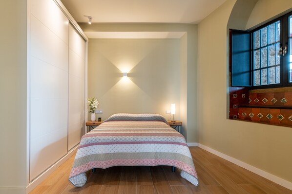 A bedroom with a bed, a nightstand, a wall-mounted light, and a window with a view. - Castilla, 1-bedroom in Triana (Sevilla)