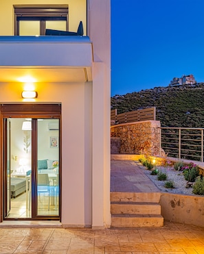 Un bâtiment moderne doté d’une entrée avec une porte en verre, d’un mur en pierre et d’un balcon donnant sur une colline.