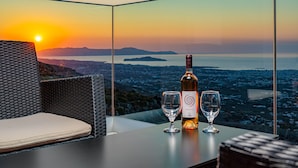 A table with a bottle of wine and two glasses, set against a backdrop of a sunset view over a cityscape. - Villa Lia with private ecologic pool and amazing view! (Kontopoula)