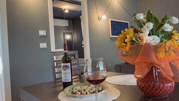 A dining table with a wine bottle, a glass of red wine, and a plate of food. There is a vase with flowers and a decorative bowl on the table.