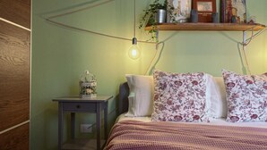 A bedroom with a bed, a nightstand, a shelf with books and a plant, and a hanging light bulb. - WellHome   "Ruchè" Apartment (ASTI)