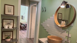 A bathroom with a round mirror, a wooden bowl sink, and a shelf with framed pictures. - WellHome   "Ruchè" Apartment (ASTI)