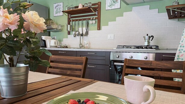 A kitchen with a dining table, chairs, a plate of berries, a potted plant, and a coffee maker. - WellHome   "Ruchè" Apartment (ASTI)