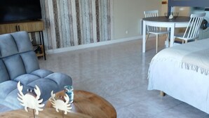 A modern living room with a sofa, a coffee table with crab decorations, a TV, a dining area with chairs, and a bed.