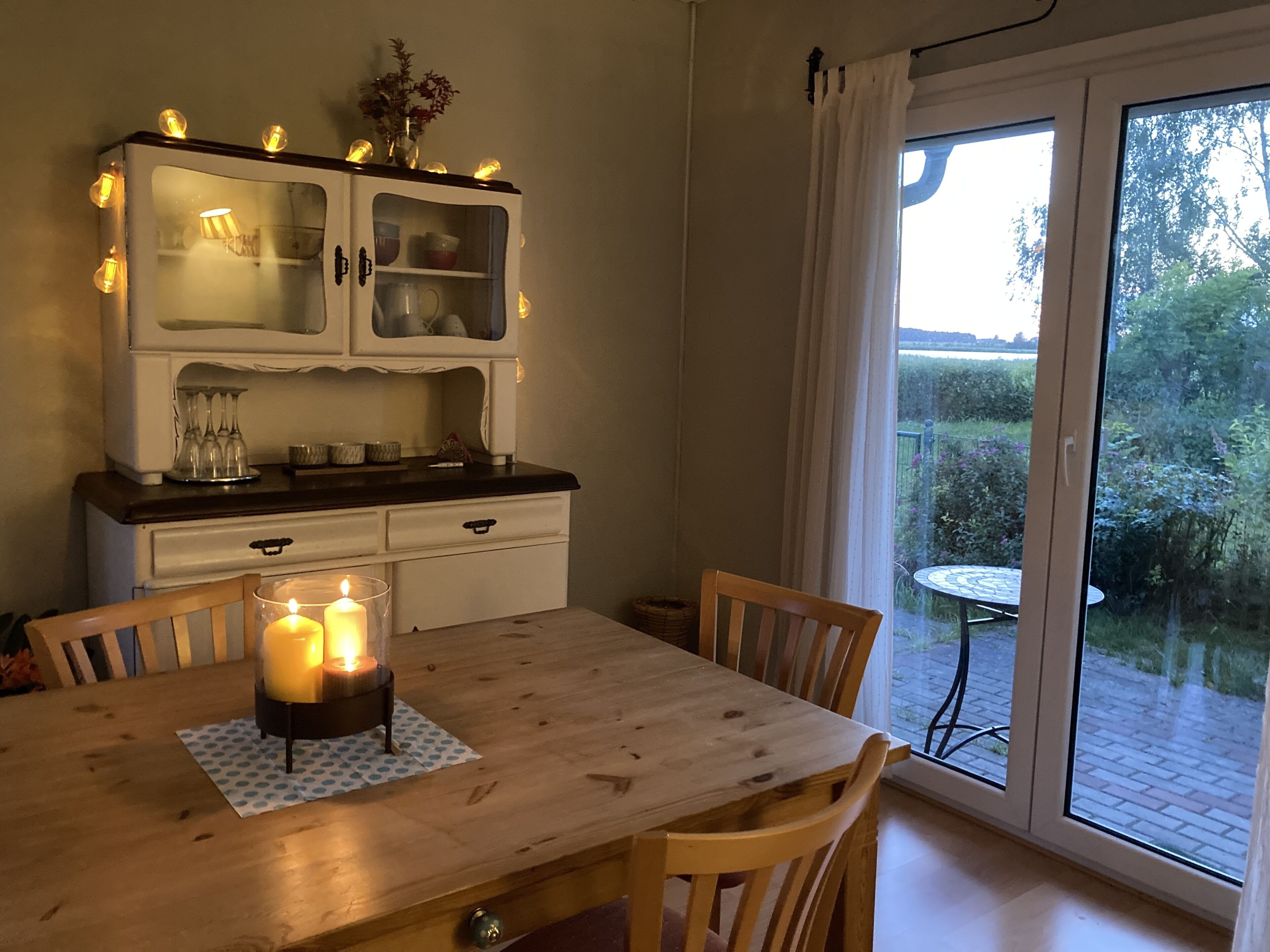 Ein Essbereich mit einem Holztisch, Stühlen, einer Kerze und einem Schrank mit Glastüren.