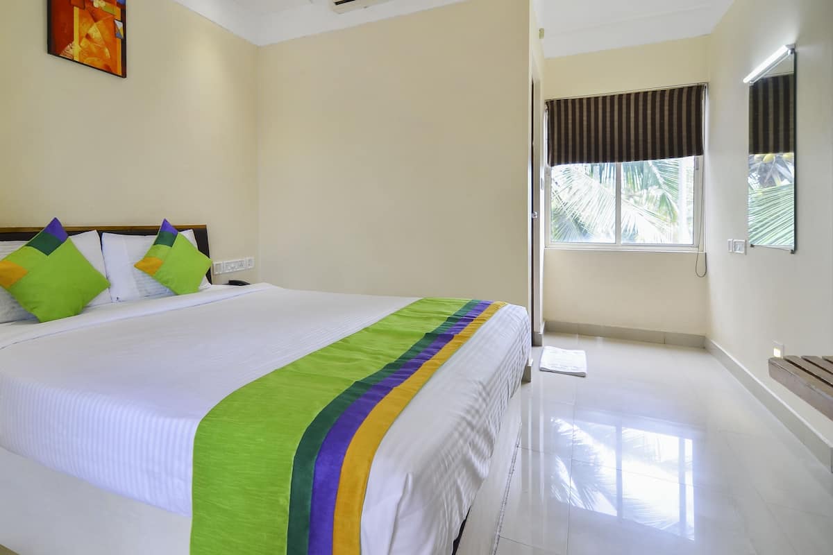A hotel room with a bed, a nightstand, a window with curtains, and a painting on the wall.