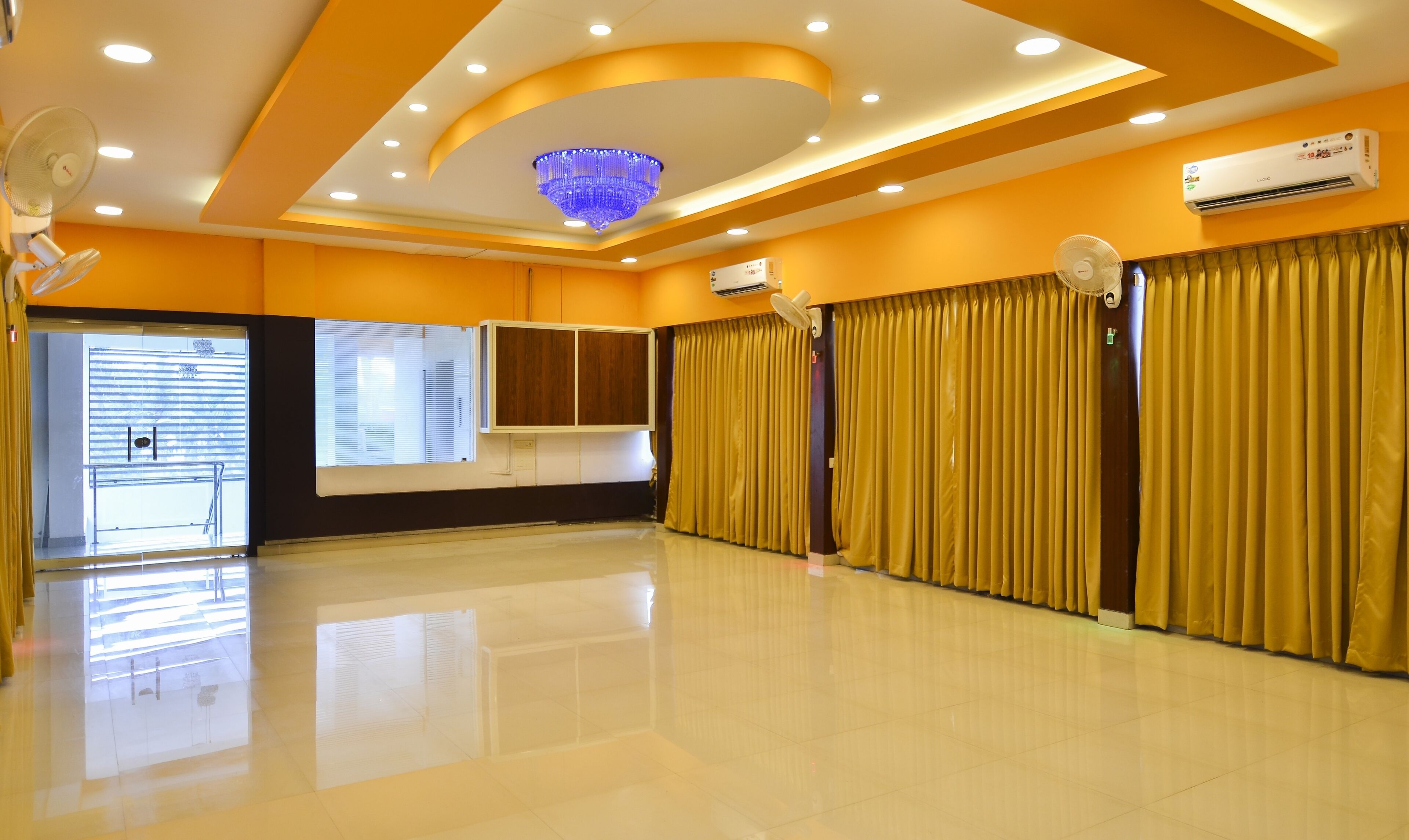 A spacious room with a large window, a ceiling fan, an air conditioning unit, and a chandelier.
