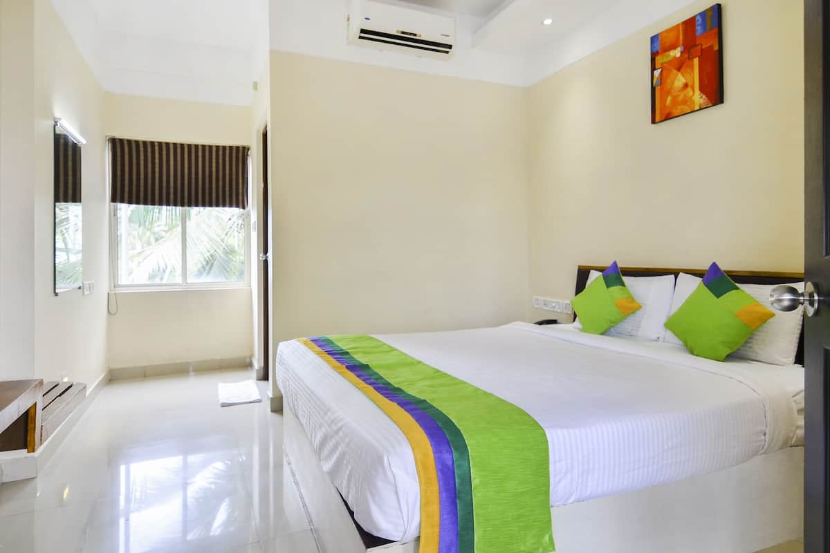 A hotel room with a bed, a window with curtains, an air conditioning unit, and a painting on the wall.