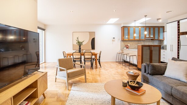 A modern living room with a flat-screen TV, a sofa, a coffee table, and a dining area with chairs and a table. - Pet Friendly - Elwood Sanctuary - walking distance to the beach (Elwood)