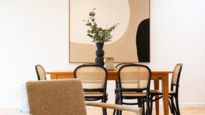 A dining area with a wooden table and four black chairs with woven seats. A potted plant is on the table, and a large abstract painting hangs on the wall. - Pet Friendly - Elwood Sanctuary - walking distance to the beach (Elwood)