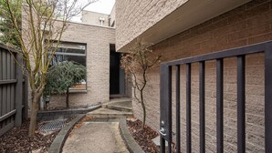 A narrow courtyard with a brick wall, a metal gate, and a small tree. - Pet Friendly - Elwood Sanctuary - walking distance to the beach (Elwood)