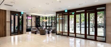 A spacious lobby with a polished floor, comfortable seating, and large glass doors leading to the street.