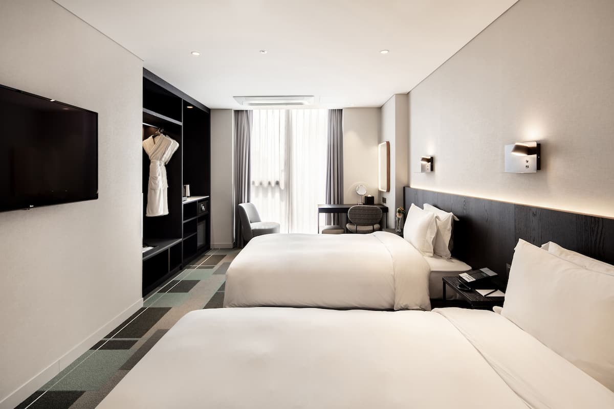 Una habitación de hotel moderna con una cama grande, un área de descanso con una silla y una mesa, un armario y un televisor de pantalla plana montado en la pared.