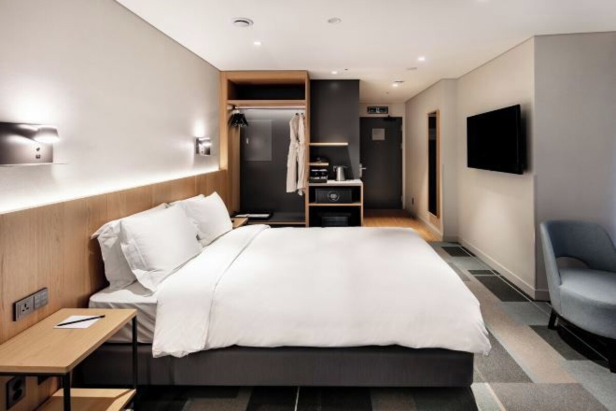 A modern hotel room with a large bed, a desk, a TV, and a wardrobe.
