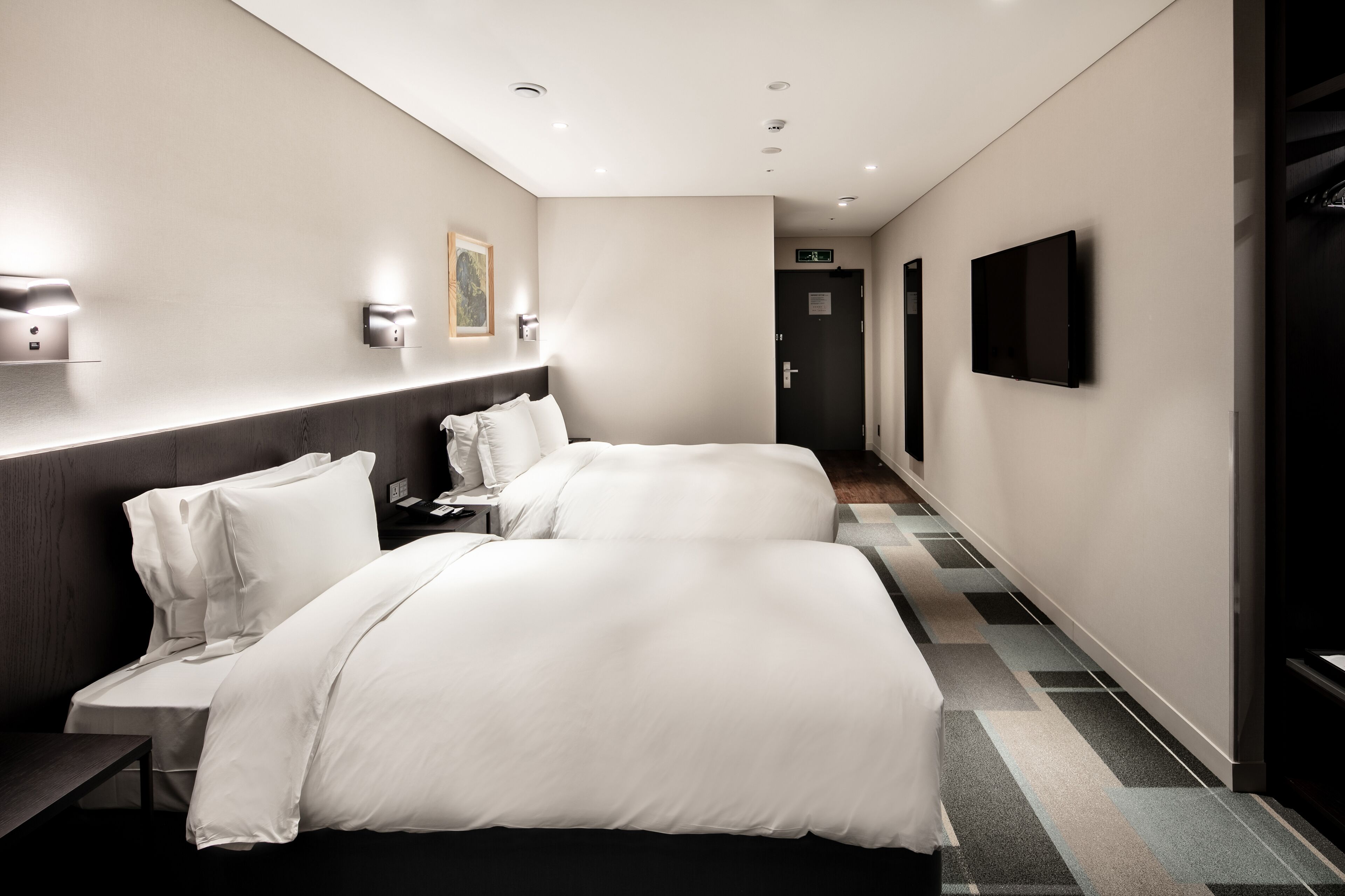 A hotel room with two beds, a desk, a chair, a flat-screen TV, and a painting on the wall.