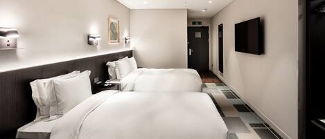 A hotel room with two beds, a desk, a chair, a flat-screen TV, and a painting on the wall.