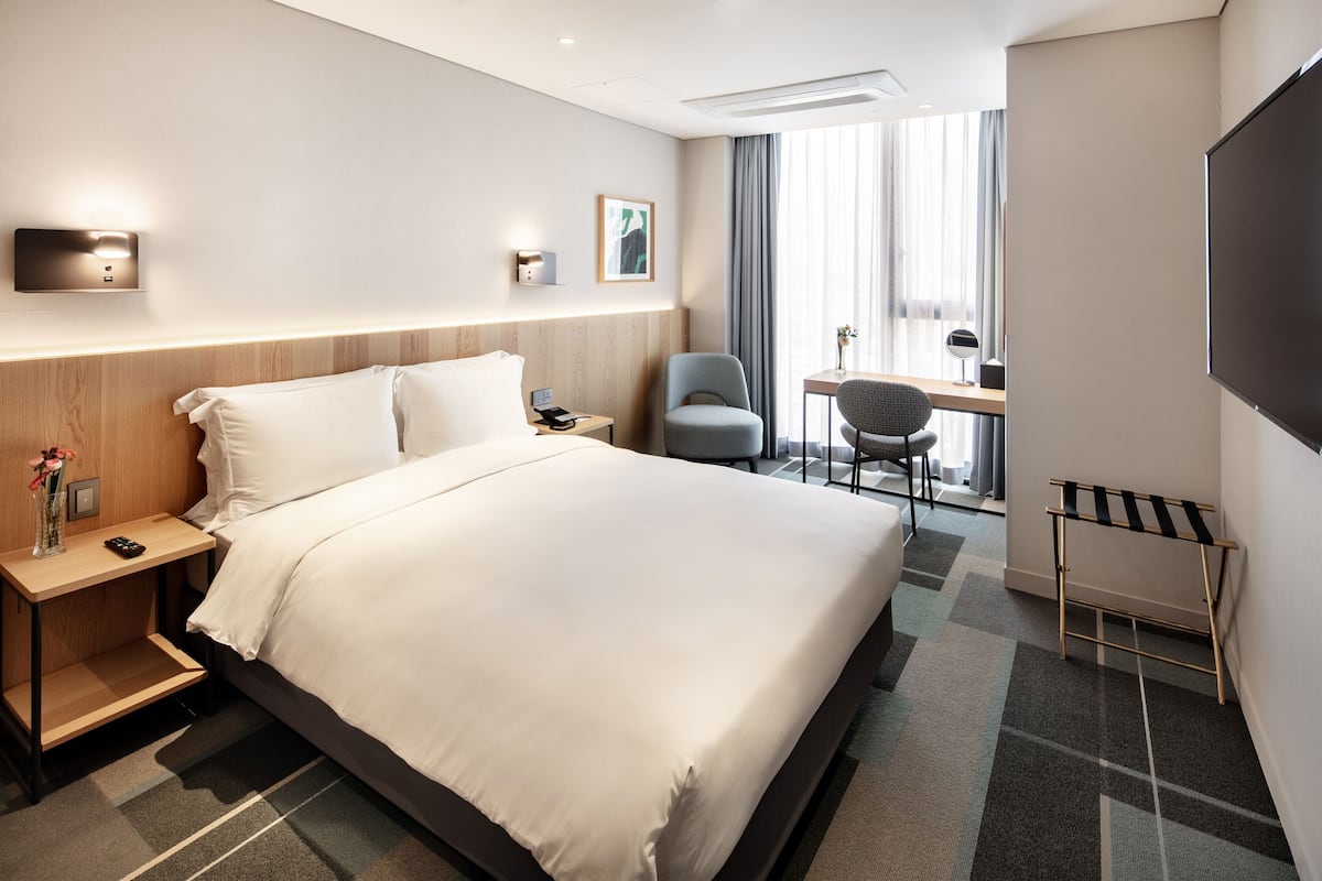 Una habitación de hotel con una cama grande, mesitas de noche, un escritorio, una silla y un televisor.