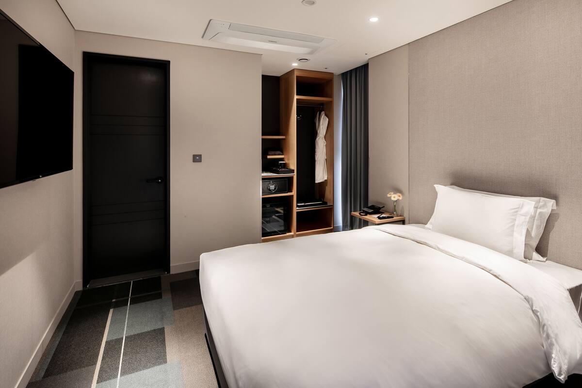 Habitación de hotel con una cama grande, un armario, un escritorio con lámpara y un televisor montado en la pared.