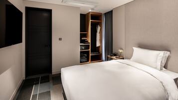 A hotel room with a large bed, a wardrobe, a desk with a lamp, and a TV mounted on the wall.