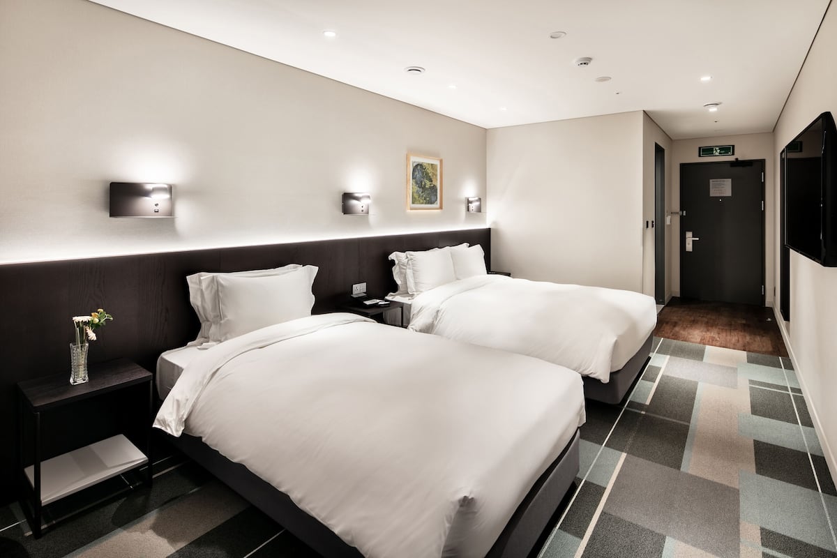Una habitación de hotel con dos camas, una mesita de noche con un florero y un cuadro en la pared.