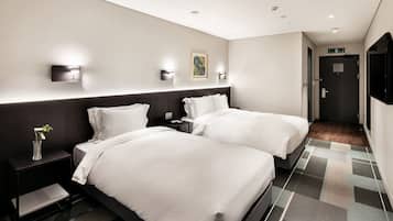 Una habitación de hotel con dos camas, una mesita de noche con un florero y un cuadro en la pared.