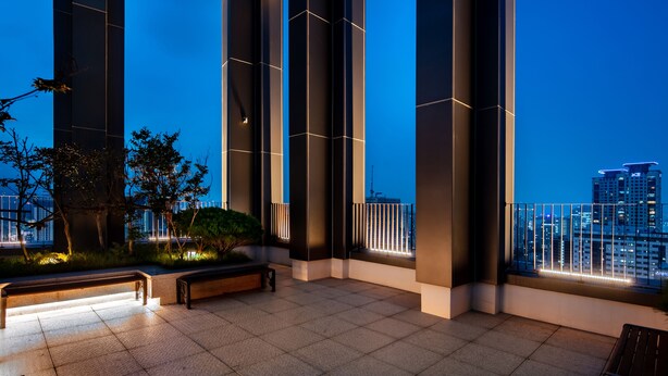 A modern building with large pillars, a bench, and a view of the city skyline at dusk. - G3 Hotel Chungmuro (Seoul)