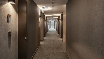 Un pasillo de hotel con piso alfombrado, puertas a ambos lados y vista a la ciudad en la distancia.