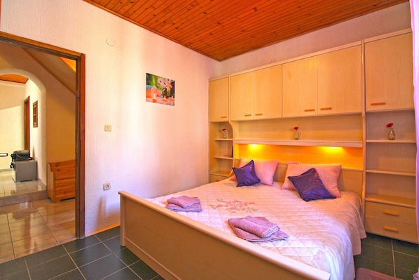 Un dormitorio con cama, cabecera de madera, estanterías empotradas con objetos decorativos y techo de madera.