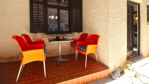 A small outdoor patio with a table and two red chairs, a window with shutters, and a door. - Apartment 2192/56814 (Istria - Pula), 3000m from the beach (Pula)