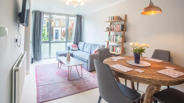 Un salon moderne comprenant un canapé, une table à manger avec des chaises, une bibliothèque et un téléviseur fixé au mur.