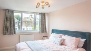 Une chambre à coucher avec un lit, des rideaux, un radiateur et une fenêtre donnant sur des immeubles.