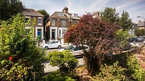 Une rue résidentielle bordée de maisons, de voitures garées et d’une végétation luxuriante.